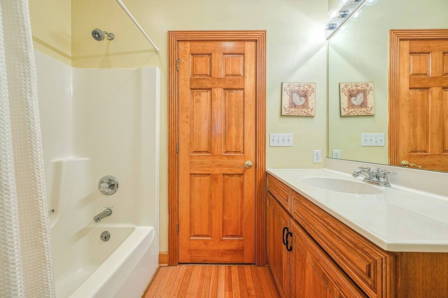A bathroom with a wooden door, a bathtub, a vanity with a sink, and a mirror.