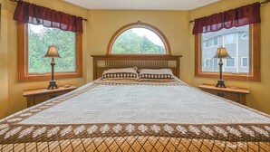 Een slaapkamer met een groot bed, twee bedlampjes en een raam met uitzicht op bomen.