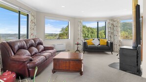 Ein geräumiges Wohnzimmer mit einem braunen Ledersofa, einem grauen Sofa mit gelben Kissen, einem Holztisch und einem schwarzen Kaminofen.