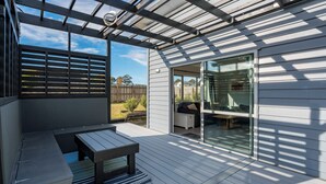 Eine überdachte Terrasse mit Holzdeck, einer Bank und einer Schiebetür zu einem Wohnbereich.