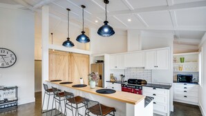 A modern kitchen with a central island, bar stools, white cabinetry, and pendant lighting. - Modern Deluxe - Havelock North Holiday Home (Havelock North)