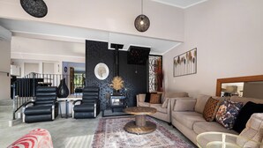 Un salon moderne avec un canapé, des fauteuils, une table basse et un tapis. On y trouve également une cheminée, un coin repas et un escalier.