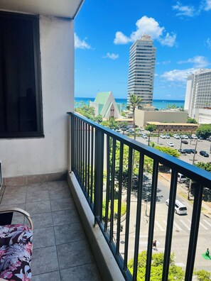 Un balcon donnant sur un parking, un immeuble de grande hauteur et un ciel dégagé.