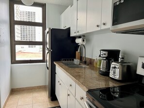 A compact kitchen with a refrigerator, stove, toaster, and a window with a view of buildings.