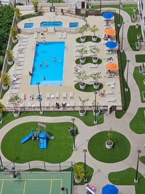 Un espace piscine sur le toit, comprenant plusieurs piscines, des chaises longues et une aire de jeux pour enfants.