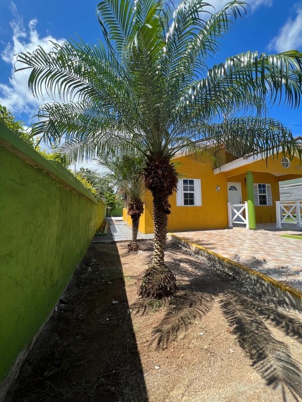 A pathway leading to a yellow building with a palm tree in the foreground. - Reddie Vacation Home at Stonebrook Vista Trelawny (Florence Hall Village)