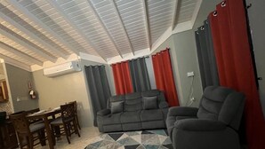 A living room with a gray sofa, a gray armchair, a dining table with chairs, and a geometric patterned rug. - Reddie Vacation Home at Stonebrook Vista Trelawny (Florence Hall Village)