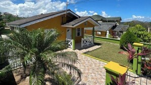 A yellow building with a green porch, surrounded by palm trees and a well-maintained lawn. - Reddie Vacation Home at Stonebrook Vista Trelawny (Florence Hall Village)