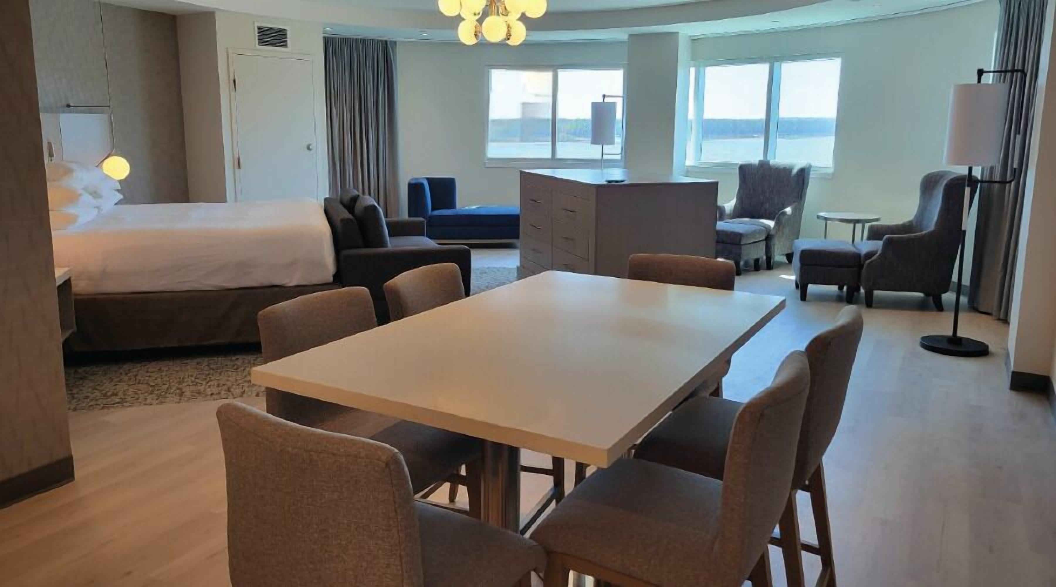 A hotel room with a bed, a dining table with chairs, a sofa, a desk, and a chair.