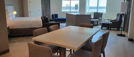 A hotel room with a bed, a dining table with chairs, a sofa, a desk, and a chair.