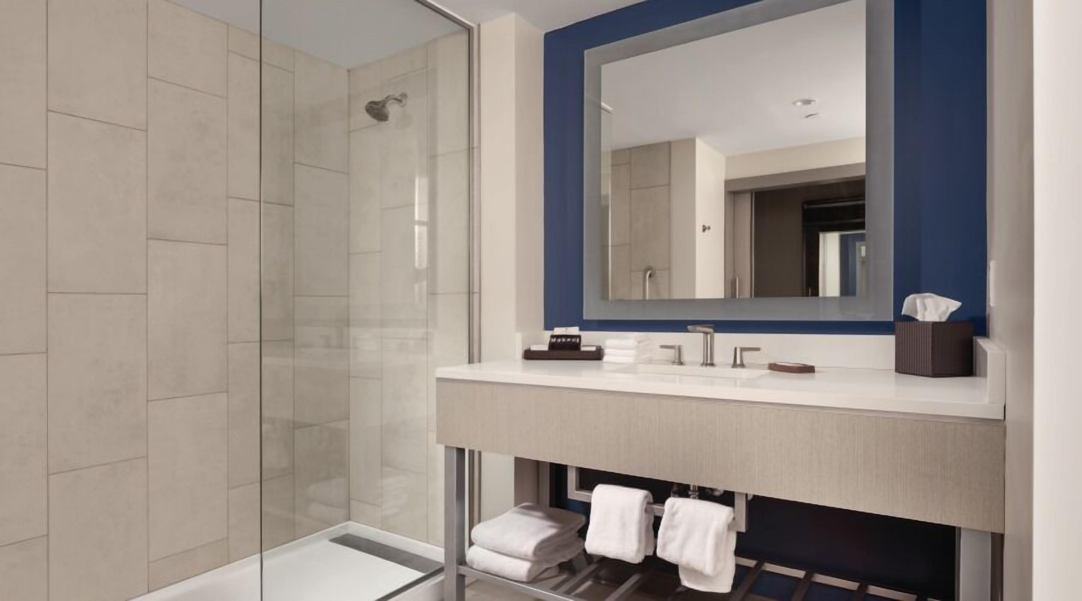 A modern bathroom with a glass shower enclosure, a large mirror, and a vanity with a towel rack.