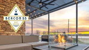 A modern outdoor seating area with a glass-top table and a fire feature, overlooking a sunset view. - The Riverview (Cape Girardeau)