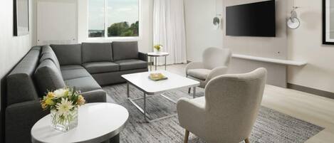 Una sala de estar moderna con un sofá seccional gris, una mesa de centro redonda, un sillón beige y un televisor de pantalla plana montado en la pared.