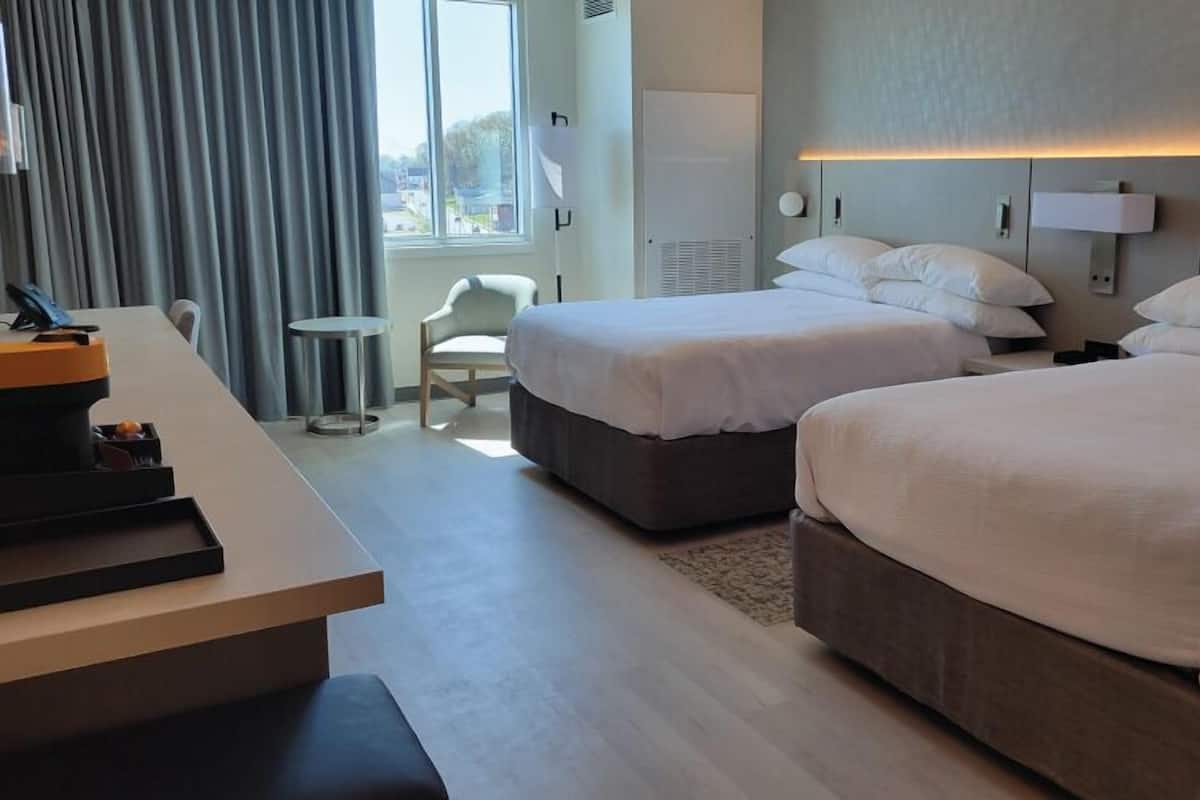 A hotel room with two beds, a desk, a chair, and a window with curtains.