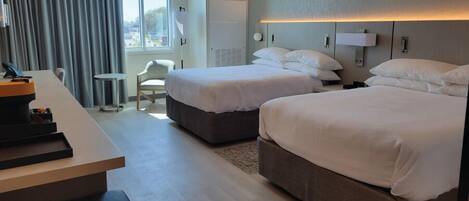 A hotel room with two beds, a desk, a chair, and a window with curtains.