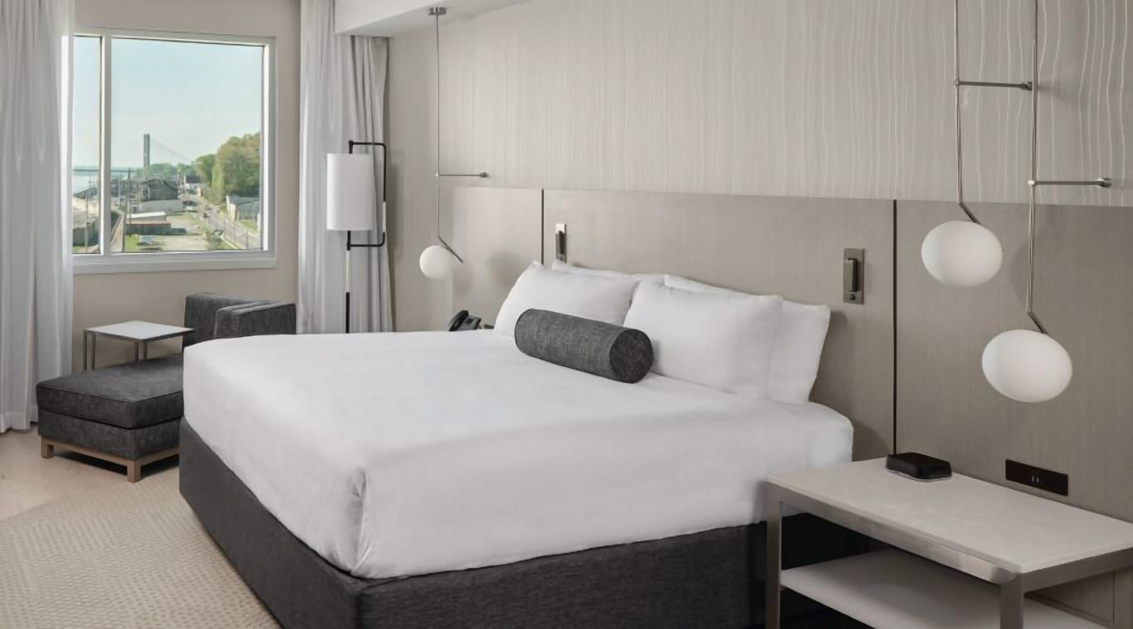 A modern hotel room with a large bed, bedside tables, a desk, and a view of the outdoors.