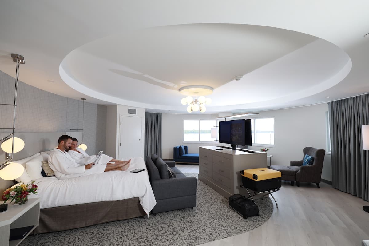 A modern hotel room with a large bed, a sofa, a desk, and a TV.