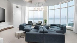 A modern living room with a large sectional sofa, a flat-screen TV, and a view of the sea through large windows. - The Riverview (Cape Girardeau)