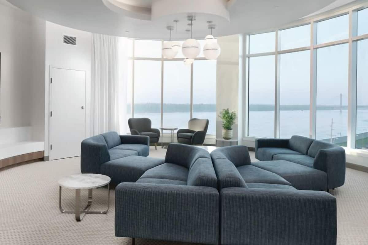 A modern living room with a large sectional sofa, a flat-screen TV, and a view of the sea through large windows.