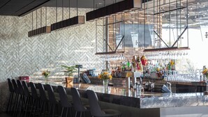 A modern bar area with a herringbone patterned wall, a long counter with bar stools, and a variety of bottles and glasses. - The Riverview (Cape Girardeau)