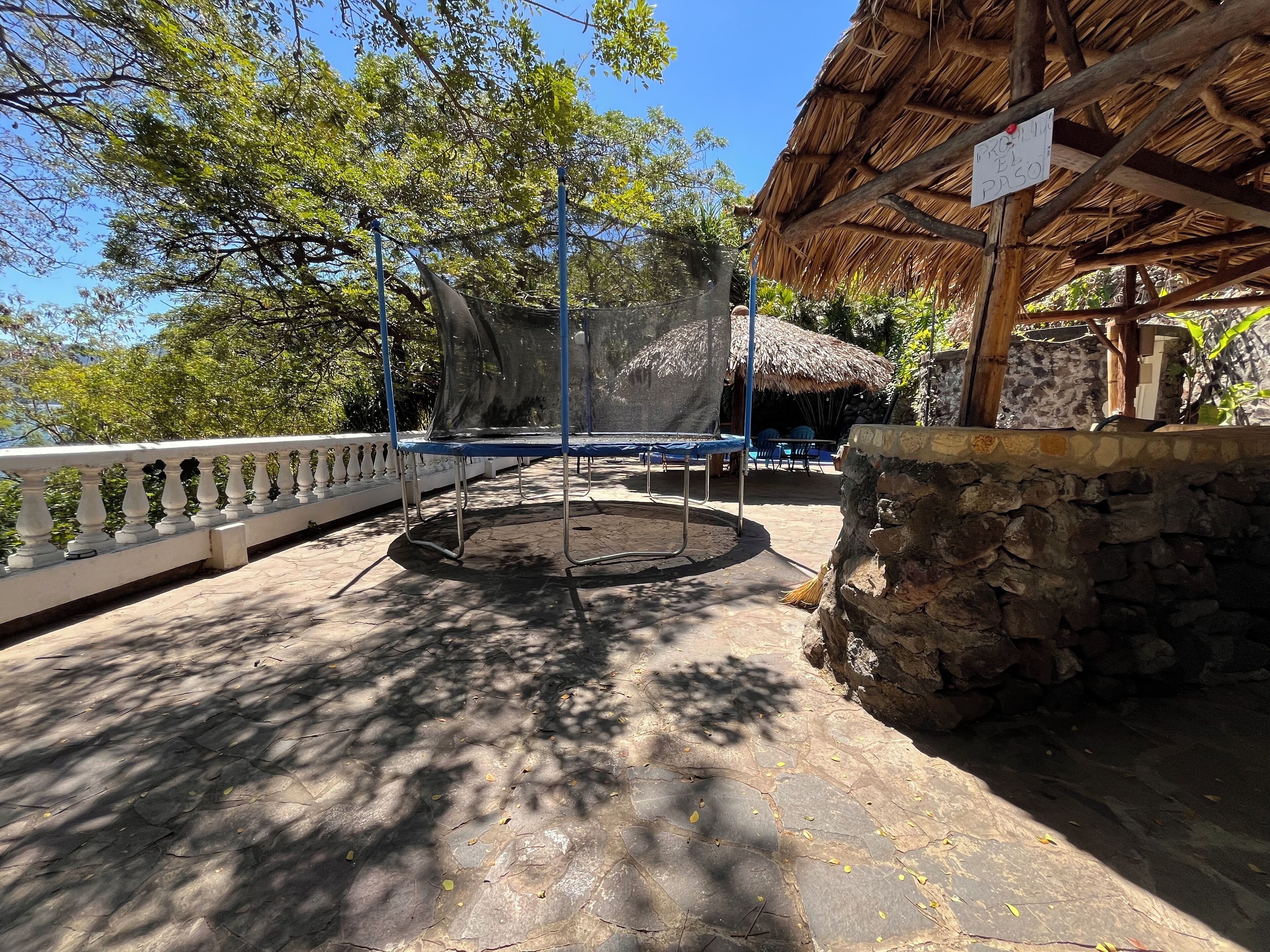 A stone-walled outdoor area with a trampoline and a thatched-roof structure.