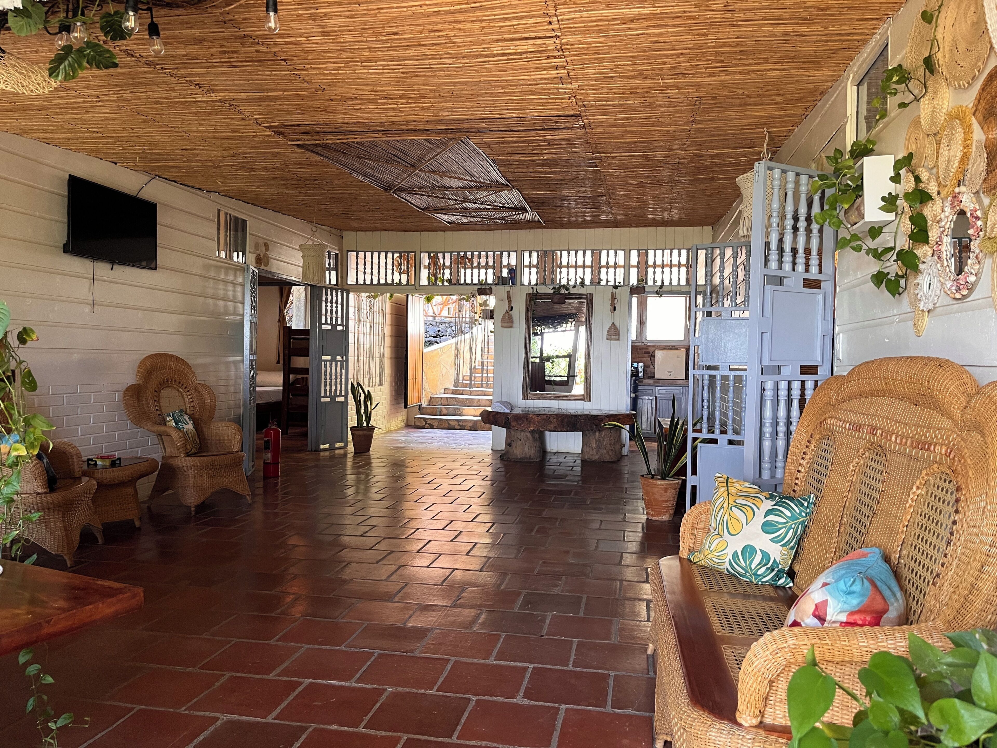 A spacious living area with wicker furniture, a brick floor, and a ceiling with a woven design.