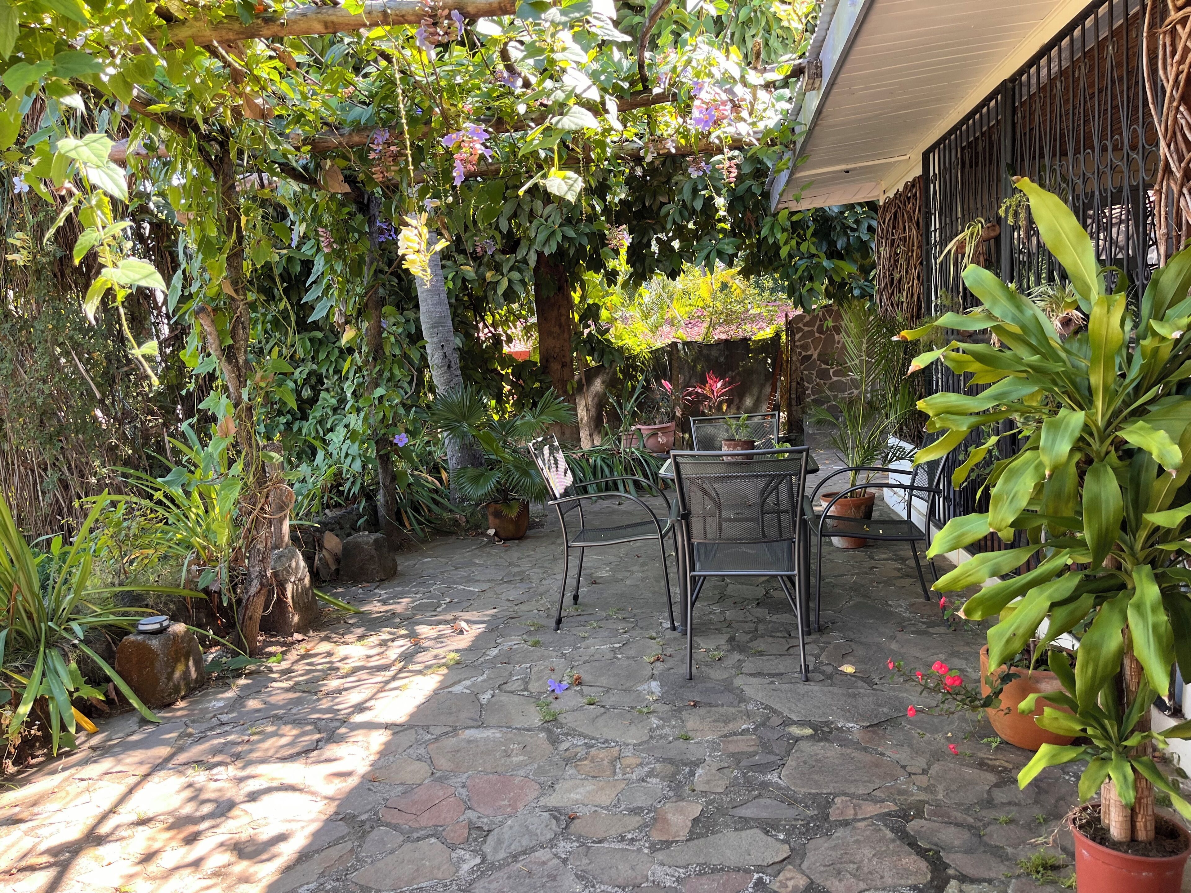 Un patio con suelo de piedra, sillas de metal y plantas en macetas.