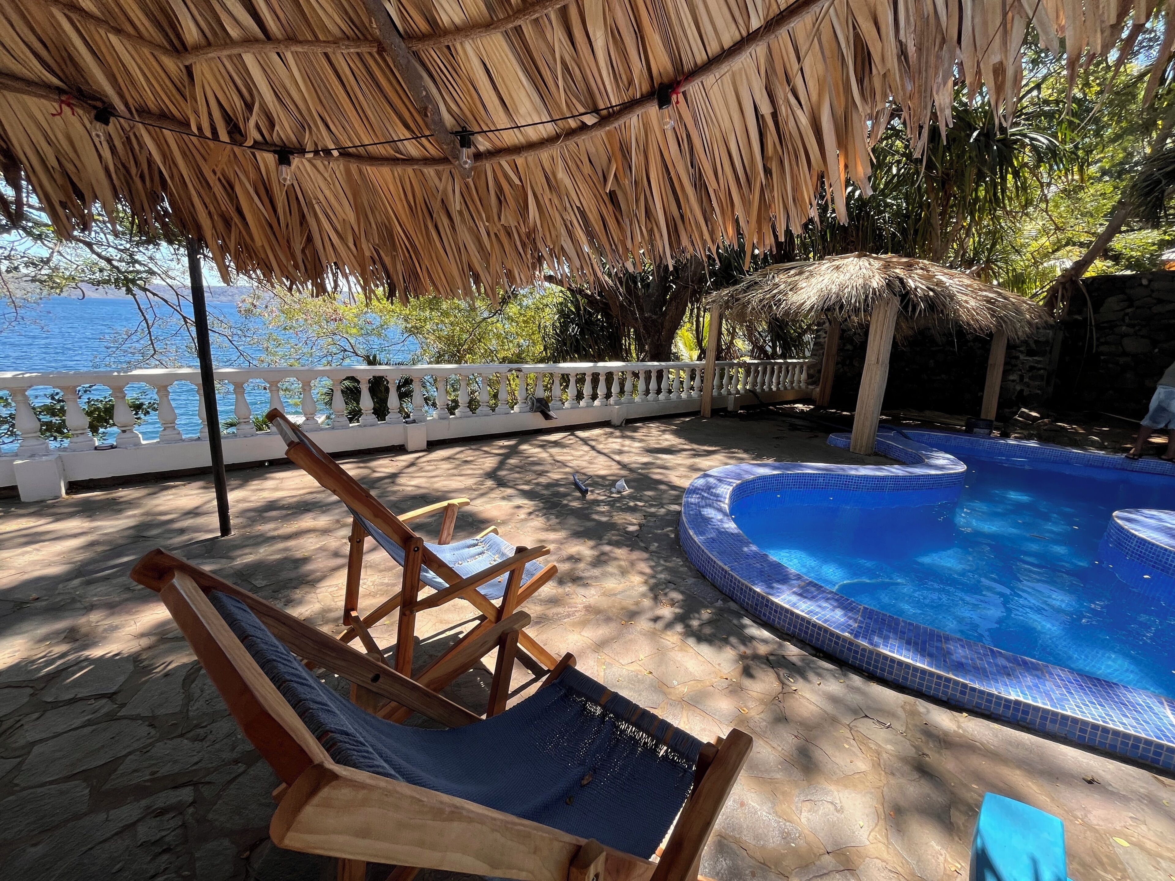 Un espace aménagé au bord de la piscine, doté d’un toit de chaume, d’une chaise longue et offrant une vue sur la mer.