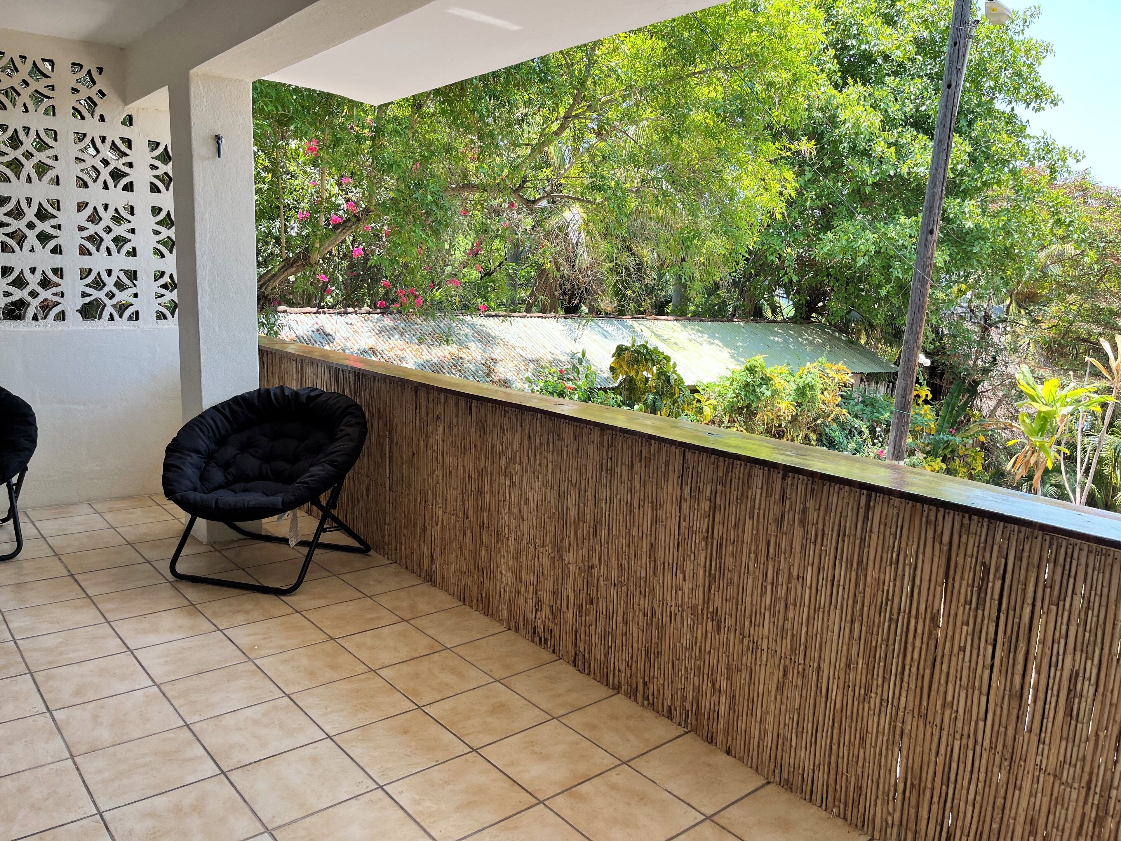 A balcony with a tiled floor, a black chair, and a bamboo wall.