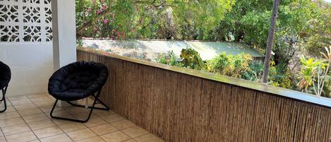 A balcony with a tiled floor, a black chair, and a bamboo wall.
