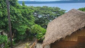 A thatched-roof hut with a stone pathway leading to it, surrounded by lush greenery and a view of a body of water.