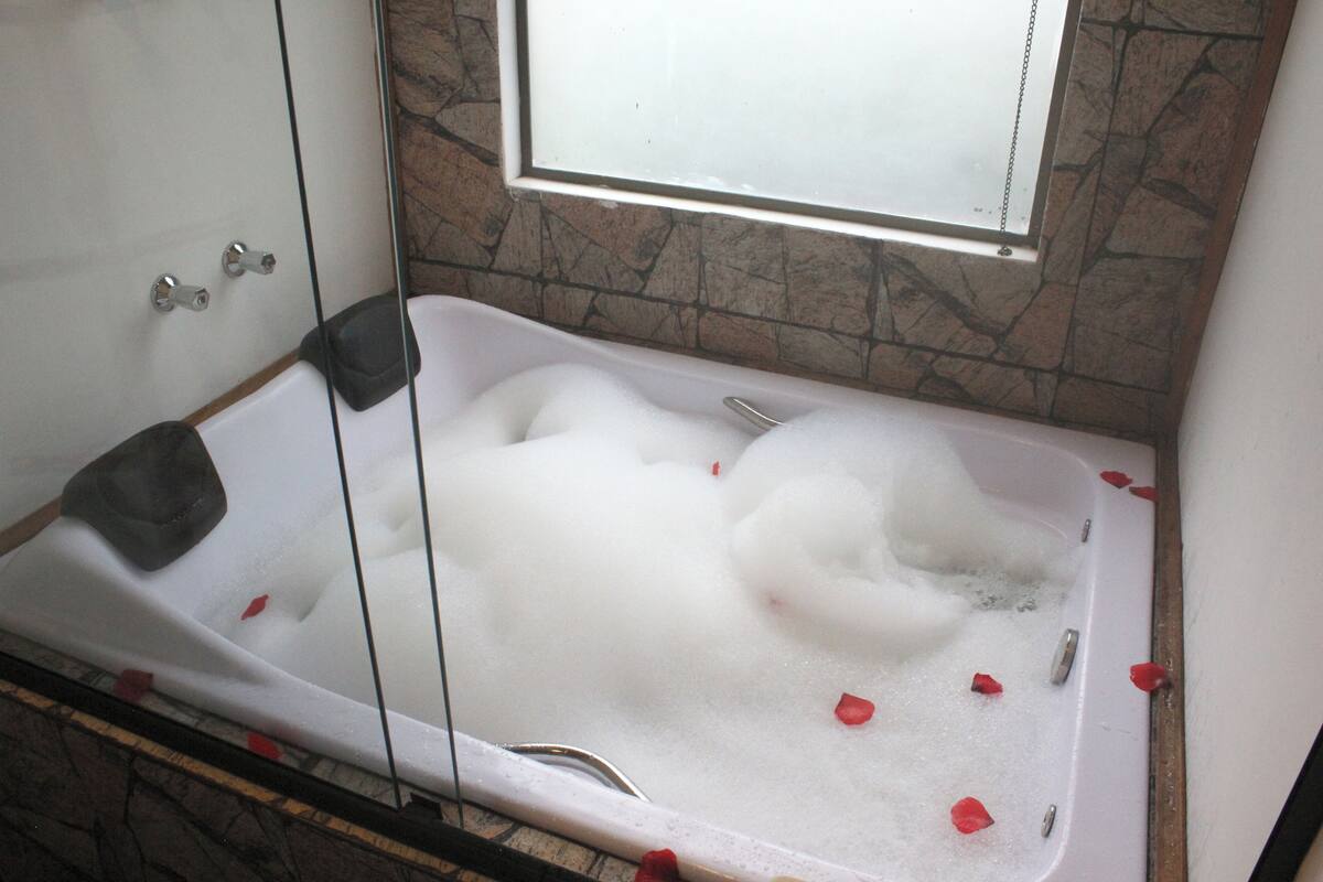 Een bad vol bubbels en rozenblaadjes, met een stenen muur en een raam erboven.