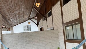 A hammock under a wooden roof structure, with brick walls and windows.