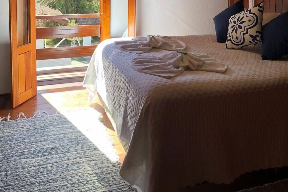 Een slaapkamer met een houten plafond, een bed met een witte dekbedovertrek, een ronde spiegel en uitzicht op groen.