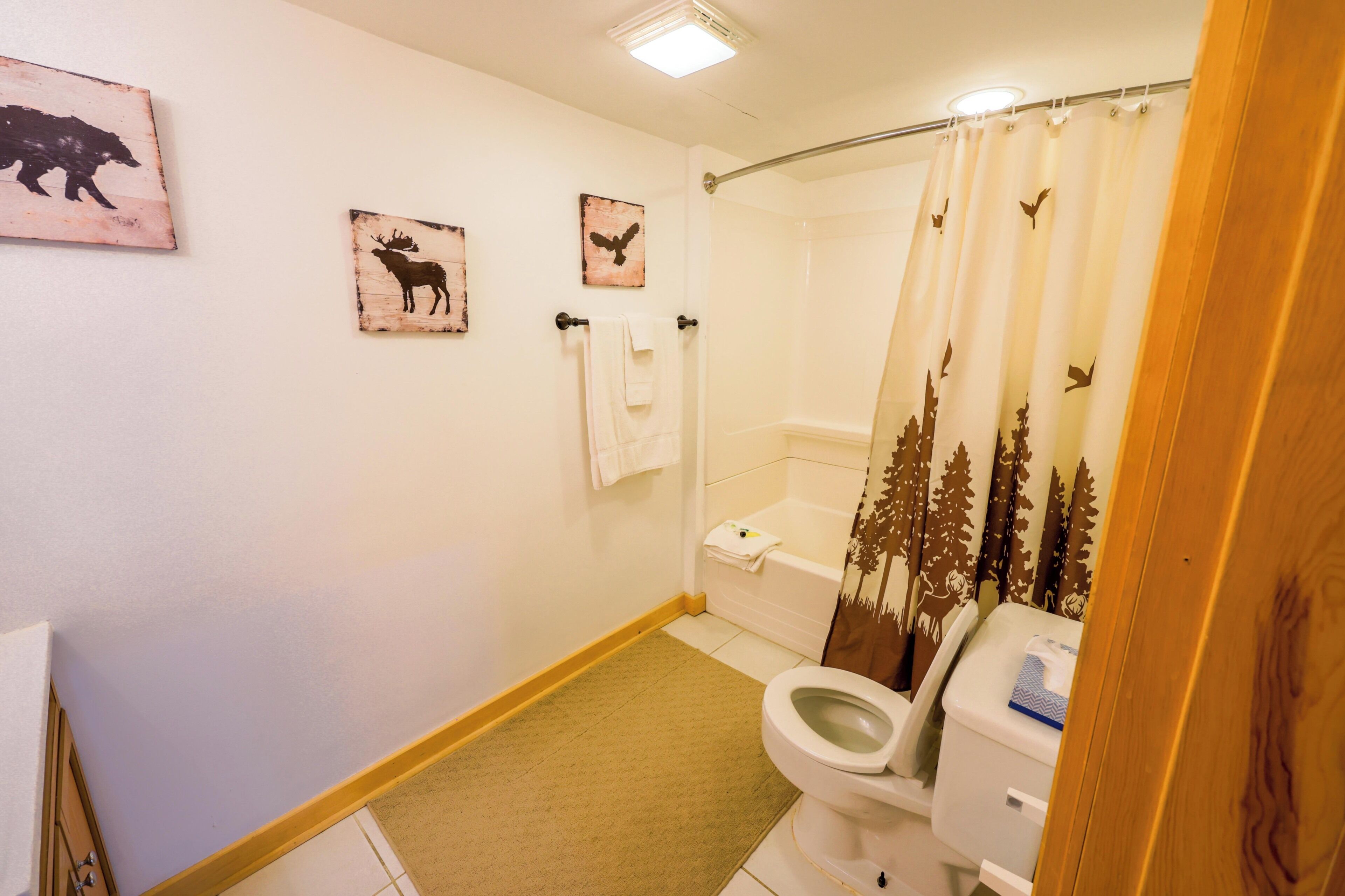 A bathroom with a toilet, shower curtain with forest design, and wall-mounted towels.