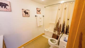 Bagno con WC, tenda da doccia con motivo forestale e asciugamani a parete.
