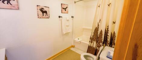 A bathroom with a toilet, shower curtain with forest design, and wall-mounted towels.