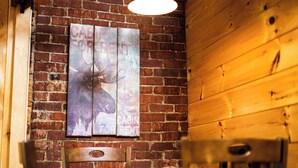 A rustic interior with a brick wall, wooden paneling, and a table with chairs. - Historic barn at Moosehead Lake (Greenville)