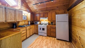 A wooden cabin kitchen with a skylight, wooden cabinets, a stove, a microwave, and a refrigerator. - Historic barn at Moosehead Lake (Greenville)