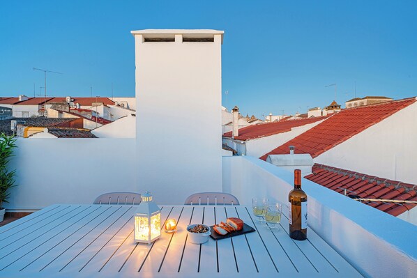 Eine Dachterrasse mit Esstisch, einer Weinflasche und einer Laterne.