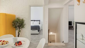 Une chambre d’hôtel moderne avec un lit, un coin repas comprenant une table et des chaises, une petite plante et un téléviseur en arrière-plan.