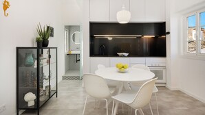 Une cuisine moderne avec des meubles blancs, un plan de travail noir et un coin repas blanc agrémenté de chaises en osier.