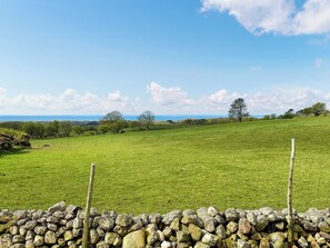 Un paysage rural avec un mur de pierres, un champ verdoyant et des arbres qui se dessinent à l’horizon.