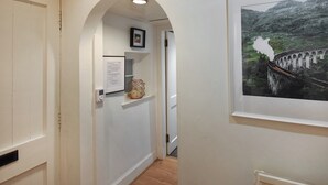 Corredor com paredes brancas, piso de madeira, quadro de uma ponte e um pequeno aparador com um objeto decorativo.