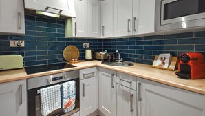Uma cozinha moderna com armários brancos, painel de azulejos azuis, eletrodomésticos de aço inoxidável e bancada de madeira.