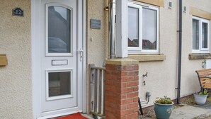Une porte blanche avec un panneau de verre, un pilier en briques et un petit paillasson rouge à l’entrée.