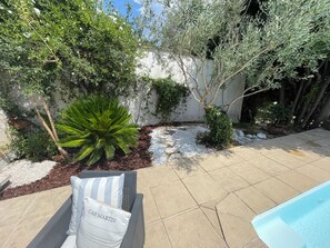 A patio area with a pool, a white wall, and various plants.