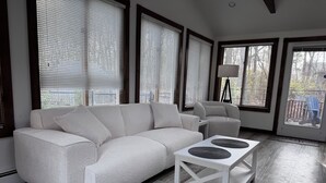 A modern living room with a white sofa, a white coffee table, and large windows with blinds. - Charming Cape Cod house in Dennis Massachusetts. Pets Friendly! (Dennis)