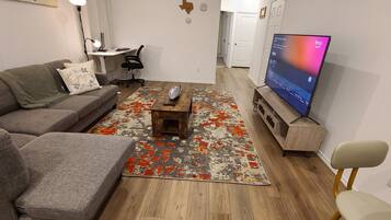 Un salon avec un canapé gris, une table basse, un téléviseur et un tapis à motifs.