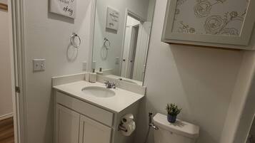 Un baño con lavamanos blanco, espejo, inodoro y una obra de arte floral enmarcada en la pared.